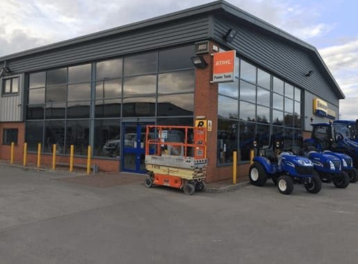 Grey industrial building with an orange "STIHL Power Tools" fascia sign, tractors parked outside.