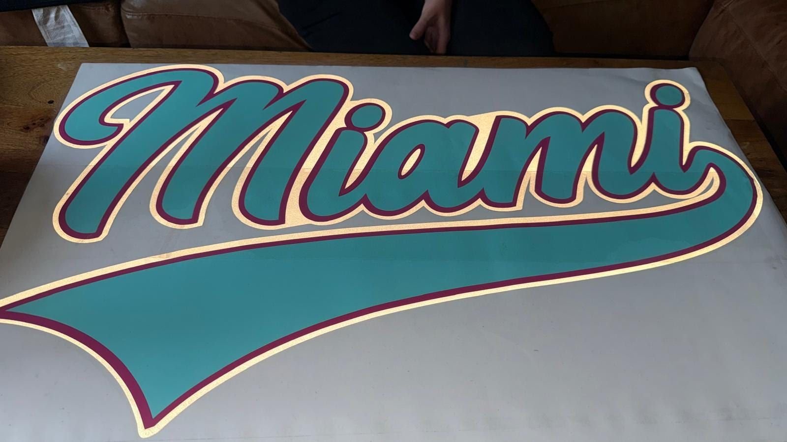 Teal, maroon and gold "Miami" script cut vinyl lettering laid out on a table before fitting.